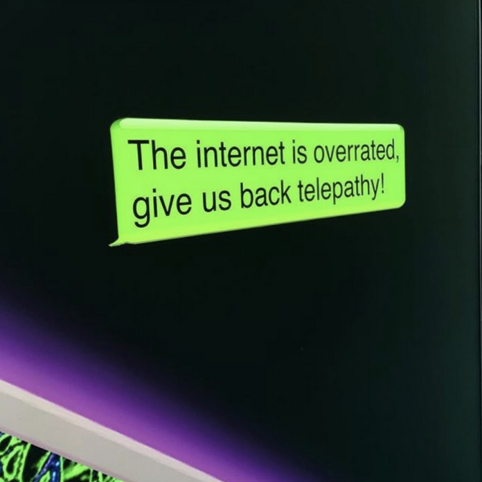 The image shows a work by Tabita Rezaire; there is a green message bubble on a dark background which reminds of outer space. The bubble reads "The internet is overrated, give us back telepathy!"